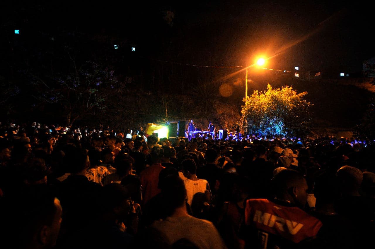 A imagem mostra uma das edições do Baile da Serra. Uma edição noturna e ao ar livre, é possível ver a multidão que frequenta o baile. Ao fundo está o palco