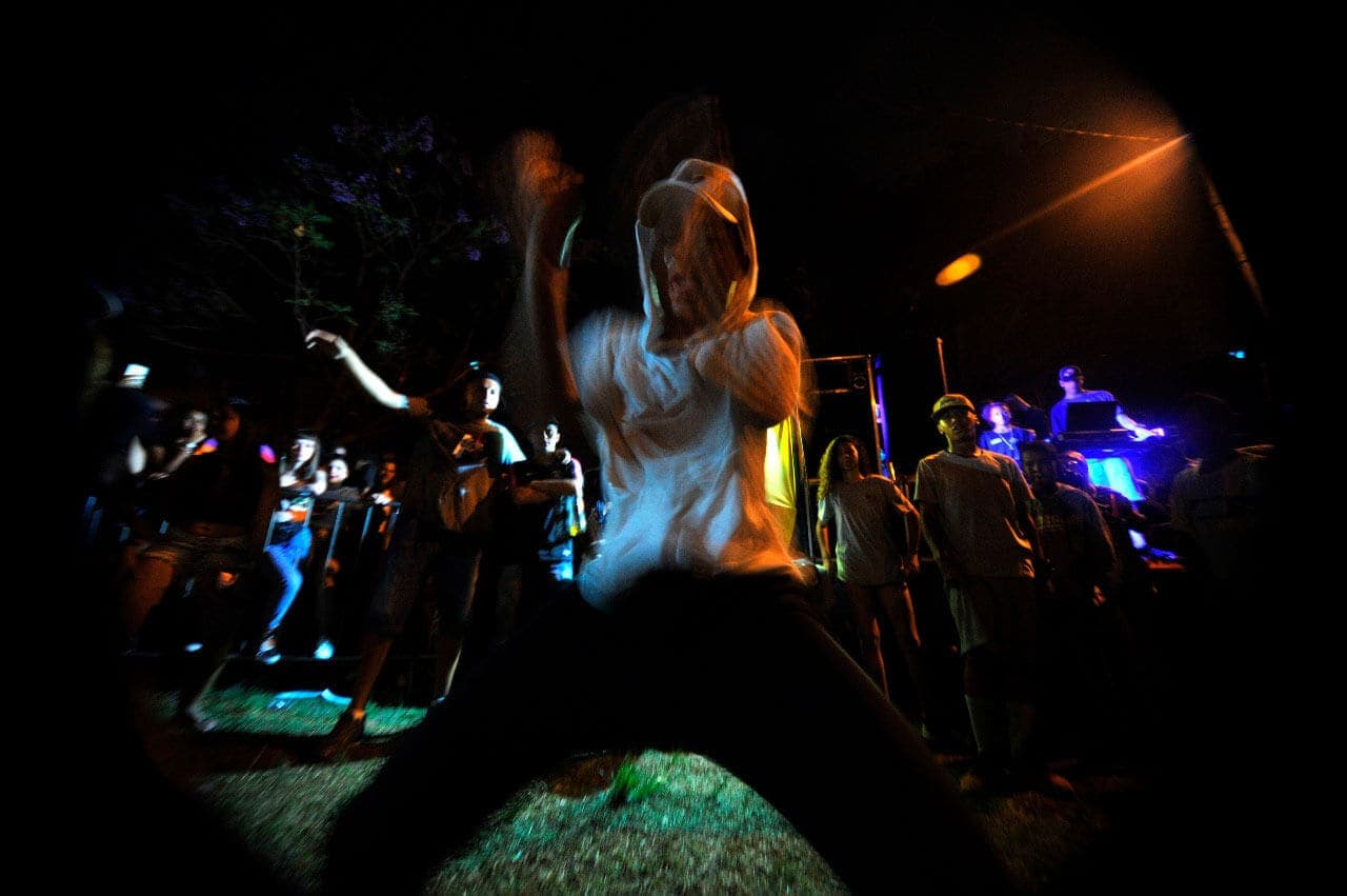 A imagem mostra um rapaz dançando em primeiro plano, em uma das edições do Baile da Serra. Não é possível visualizar seu rosto com nitidez, pois foi capturado em movimento, e seus braços aparecem borrados. É um evento noturno, e ao fundo é possível visualizar outros participantes do evento.